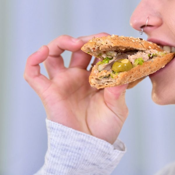 Close-up of a woman biting a delicious looking tuna sandwich with olives and anchovies on an out of focus light background.